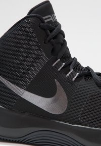 Czarne sportowe buty posiadające siateczkową i syntetyczną cholewkę, okrągłe sznurowadła oraz metalicznie srebrny znak Nike. Teksturowana podeszwa dla lepszej przyczepności.