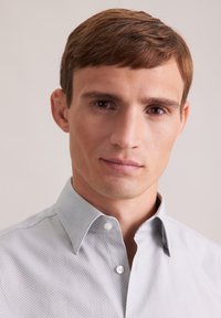Camicetta button-up grigia chiara a fantasia con colletto sottile, caratterizzata da piccoli motivi geometrici e un tessuto liscio e strutturato.