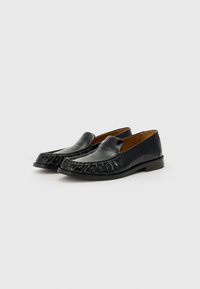Mustade nahast loafers, millel on ümar ninnt, esiosas tõstetud fringiDETAIL ja tasa kand. Sile tekstuur ja lihtne disain.