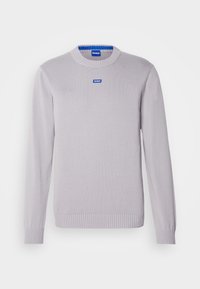 Pull gris clair à manches longues et col rond, avec poignets et ourlet côtelés, présentant un petit écusson bleu "HUGO" sur la poitrine et à l'intérieur du col.