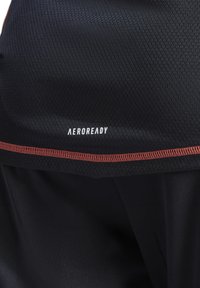 Zwart sporttop van textuur mesh stof, met een oranje accent langs de zoom. "AEROREADY" logo prominent weergegeven.
