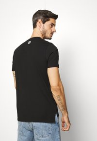 Sort kortærmet t-shirt med rund hals og sideskår, med et lille logo på ryggen. Bomuldsstof, afslappet pasform.