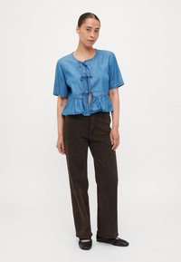 Denim peplum top s kratkimi rokavi, okroglo ovratnico in dekorativnimi zavezujočimi trakovi spredaj. Ujemite ga z temno rjavimi, ohlapnimi hlačami in črnimi balerinkami.