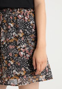 Svart blommig kjol med flera färger, elastisk midja och ett lätt, genomskinligt tyg med en flödande design.