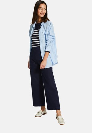 Chemise boutonnée bleu clair sur un haut rayé marine, assortie à un pantalon large marine et des mocassins crème.