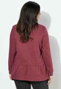 Top de manga larga burdeos con dobladillo peplum fruncido y tejido texturizado. Presenta un escote redondeado y mangas ajustadas.
