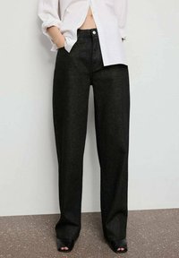 Pantalones de pierna ancha negros hechos de un tejido texturizado con un ligero brillo. Cuentan con un cierre de botón y bolsillos laterales para mayor practicidad.