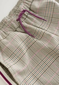 Shorts en tissu à carreaux marron et beige avec des lignes roses, taille élastique et cordon de serrage violet à nouer.