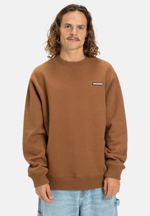 Sudadera marrón con puños y dobladillo acanalados, que presenta un pequeño parche negro de logo en el pecho. Diseño de cuello redondo con una textura suave.