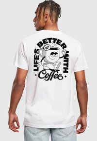 Hvit bomulls T-skjorte med en svart grafikktrykk på baksiden som har teksten "LIVET ER BEDRE MED Kaffe" og en tegneseriefigur av en kaffekopp.