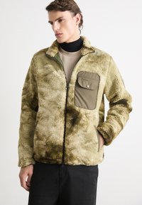 Fleece jack in olijfgroen met een getextureerde, pluche buitenkant. Beschikt over een rits aan de voorkant, zijzakken en een contrasterende utility-stijl borstzak.
