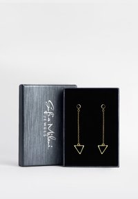 Guldtriangulära hängande örhängen med svarta accenter, visade i en grå låda klädd med svart sammet som har en silverlogotyp.