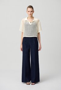 Haut en crochet crème avec un col et des manches courtes, associé à un pantalon large marine à boutons et à rayures texturées.