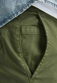 Tessuto verde oliva con una finitura strutturata, dotato di una tasca posteriore e una cucitura visibile. Parte superiore parzialmente coperta da tessuto denim blu sbiadito.