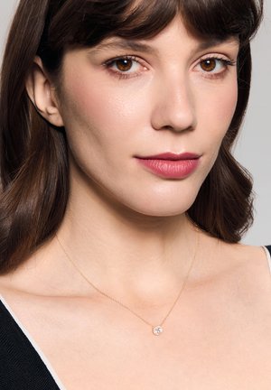 Złoty łańcuszek z okrągłym wisiorkiem i centralnym przezroczystym kamieniem szlachetnym. Prosty design z delikatną fakturą i wypolerowanym wykończeniem.