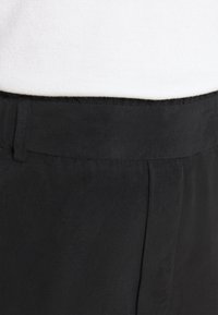 Zwarte corduroy broek met een soepele tailleband, uitgerust met een subtiele ribbelstructuur en nette voormouwen. Het materiaal lijkt zacht en duurzaam.
