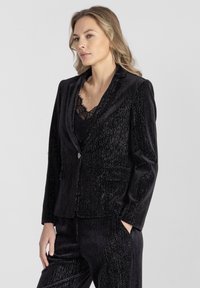 Czarna aksamitna marynarka o eleganckim kroju, teksturowanym wykończeniu, klapach z satyny i pojedynczym zapięciu na guzik z dwoma przednimi kieszeniami.