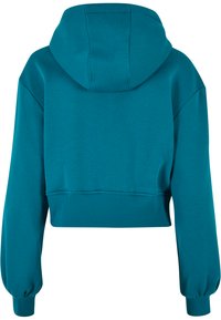 Skraćena dukserica u teal boji, napravljena od mekanog materijala. Ima kapuljaču, duge rukave s elastičnim manžetama i rebrastim porubom. Glatka tekstura.