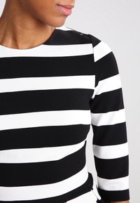 Haut à manches longues rayé noir et blanc avec un col rond ; présente des rayures épaisses contrastées et une texture de tissu lisse.