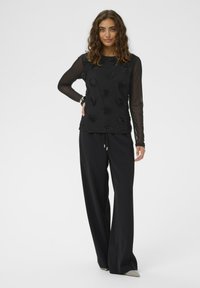 Melna garā piedurkne topam ir teksturēti ziedu akcenti un caurspīdīgas piedurknes. Saskaņots ar brīviem melniem biksēm un smailiem apaviem.