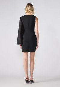 Svart klänning med en lång genomskinlig ärm. Figursydd siluett, knälång, slätt material, dragkedjestängning i ryggen, minimalistisk design.