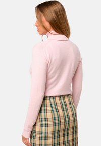 Un pull à col roulé rose clair en tissu doux, au design ajusté, avec des poignets côtelés, associé à une jupe à carreaux en beige, vert et rouge.