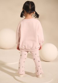 Rosa Sweatshirt mit abgerundetem Saum, kombiniert mit rosa gerippten Hosen mit floralem Muster, beide aus weichem, strukturiertem Stoff gefertigt.