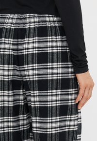 Sorte og hvide ternede bukser med elastisk talje, der har en børstet tekstur og en afslappet pasform, og præsenterer et klassisk tjekmønster.