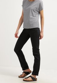 Top corto a righe grigie e bianche con maniche corte abbinato a pantaloni neri slim-fit e sandali neri. Presenta una tasca sul lato sinistro del top.