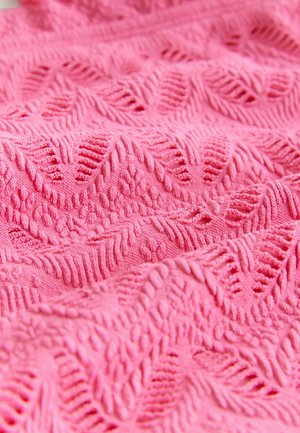 Roza pletenina z teksturiranim zigzagovim vzorcem, ki vsebuje dvignjene niti in prepletene motive, se ponaša z mehkobo in elastičnostjo.