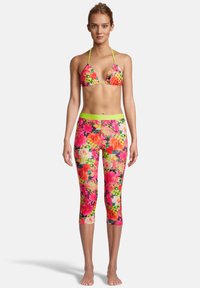 Haut de bikini fleuri et leggings capri en rose vif, vert et jaune. Le matériau semble élastique ; il présente de grands motifs de fleurs et des bordures accentuées.