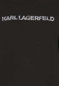 Camiseta de tela negra con el logo blanco texturizado "KARL LAGERFELD" en el pecho, con una tipografía llamativa y casual.