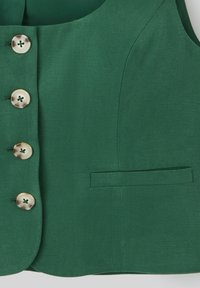 Gilet sans manches vert à la texture lisse, comportant cinq grands boutons crème et une petite poche à gauche.