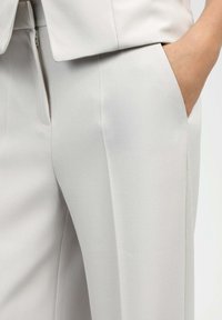Pantalon sur mesure gris clair en tissu lisse, doté d'une poche latérale et d'une fermeture éclair dissimulée, avec une coupe droite élégante.
