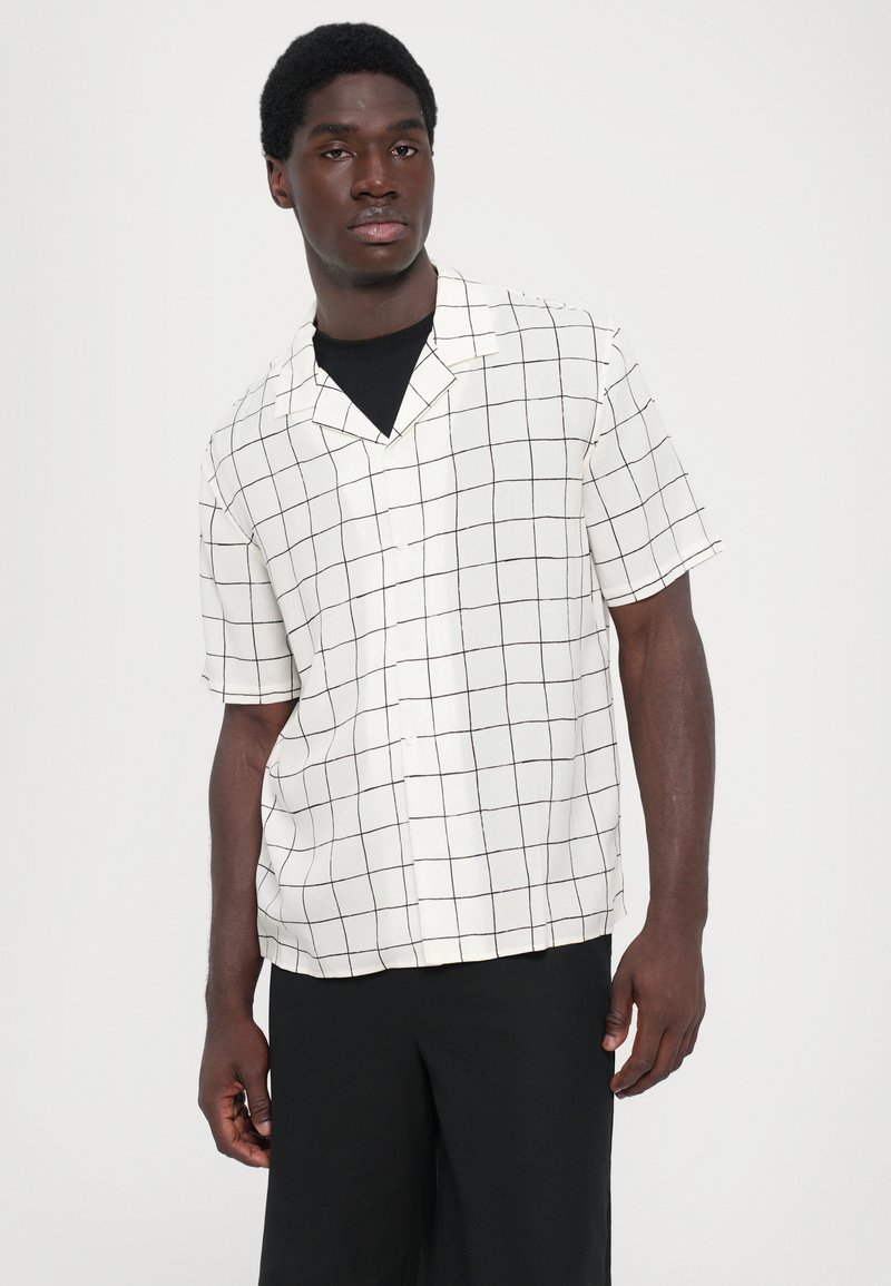 Kortärmad skjorta med knäppning i krämfärg med ett svart rutmönster, med en avslappnad krage och ett lätt, strukturerat tyg.
