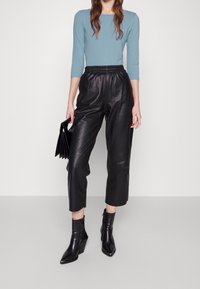 Ljusblå långärmad topp, svarta fusk läder croppade byxor med elastisk midja, svarta ankle boots, håller en svart kuvertväska.