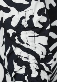 Tessuto a pattern bianco e nero con un design mimetico; la vista ravvicinata mostra i dettagli delle cuciture arricciate sulla manica. Materiale morbido e leggero.