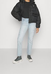 Svart puffjacka med huva, svart långärmad skjorta, ljusblå jeans med dekorativa detaljer, och grå höga sneakers.