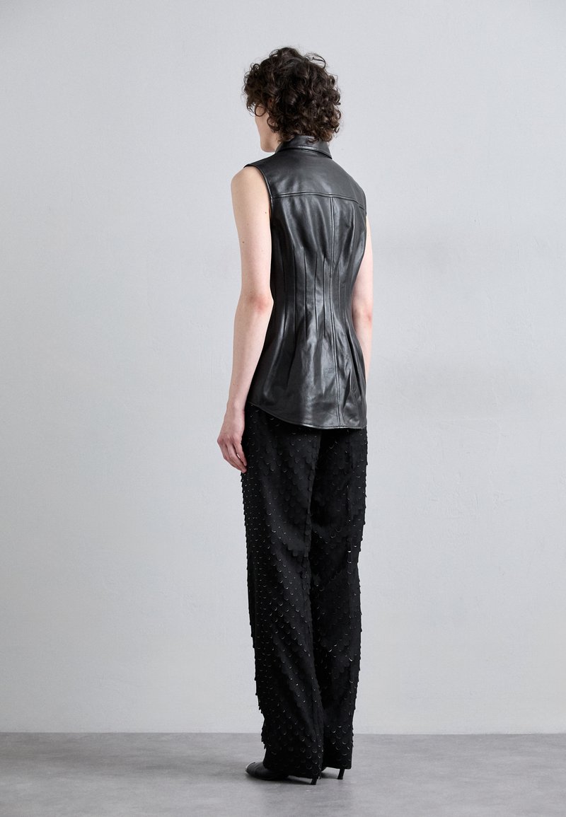 Haut sans manches en cuir noir avec un design ajusté, featuring des coutures verticales. Associé à un pantalon noir texturé avec un motif en écailles.