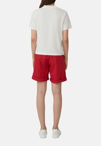 Witte korte mouwen polo shirt gecombineerd met rode shorts, opgerolde mouwen en witte sneakers, gezien van achteren. Vlotte stofstructuur.