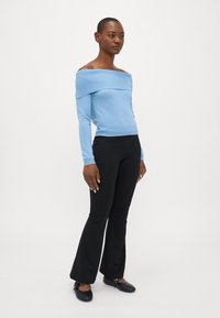 Ljusblå off-shoulder-tröja med ribbad textur, kombinerad med svarta utsvängda byxor och svarta platta skor med dekorativa detaljer.
