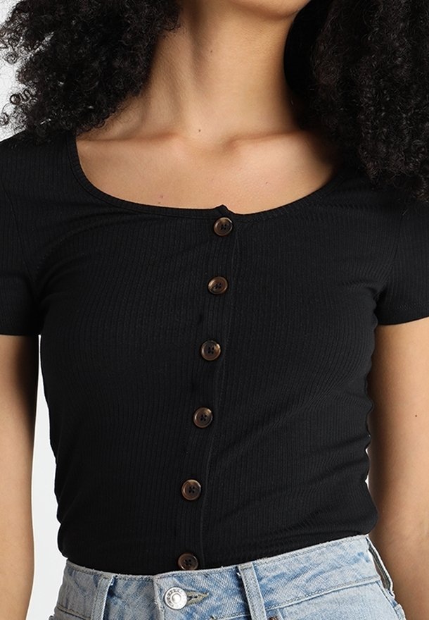 Svart ribbat kortärmad topp med rund halsringning och sju bruna knappar nedtill i mitten. Tyget verkar mjukt och figurnära.
