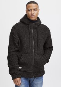Black fleece hoodie with a textured, fuzzy surface; features a front zipper, adjustable drawstrings, and large pockets.