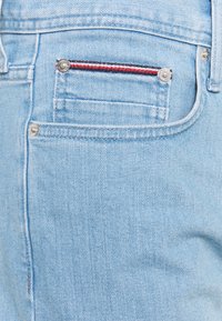 Jasnoniebieska tkanina dżinsowa z tylną kieszenią ozdobioną czerwonym, białym i niebieskim szwem oraz metalowym guzikiem.