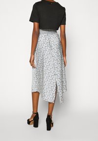 Femme portant un haut noir à manches courtes avec une jupe midi à motifs bleus et blancs taille haute et des sandales noires à talons hauts.