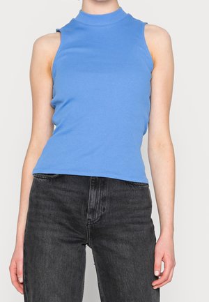 Top sin mangas de color azul claro con cuello alto y cortes en los hombros, combinado con jeans gris oscuro. Textura suave, diseño ajustado.