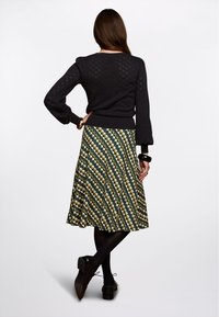 Mustat neulottu neule, jossa on teksturoitu kuvio ja puffi hihat, yhdistettynä kuvioituun vihreä-keltaiseen A-linjaiseen hameeseen. Mustat kengät ja asusteet.