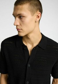 Polo shirt nero a maniche corte con chiusura a pulsante e motivo a maglia testurizzato. Presenta un colletto classico e un design traspirante.