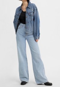 Blå denimjacka med en lös passform, framfickor och mindre slitna detaljer, i kombination med högmidjade ljusblå vida jeans.