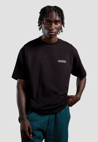 Zwart katoenen t-shirt met korte mouwen en een ronde halslijn, voorzien van een kleine witte graphic met de tekst "POCKIES" op de linkerkant van de borst.